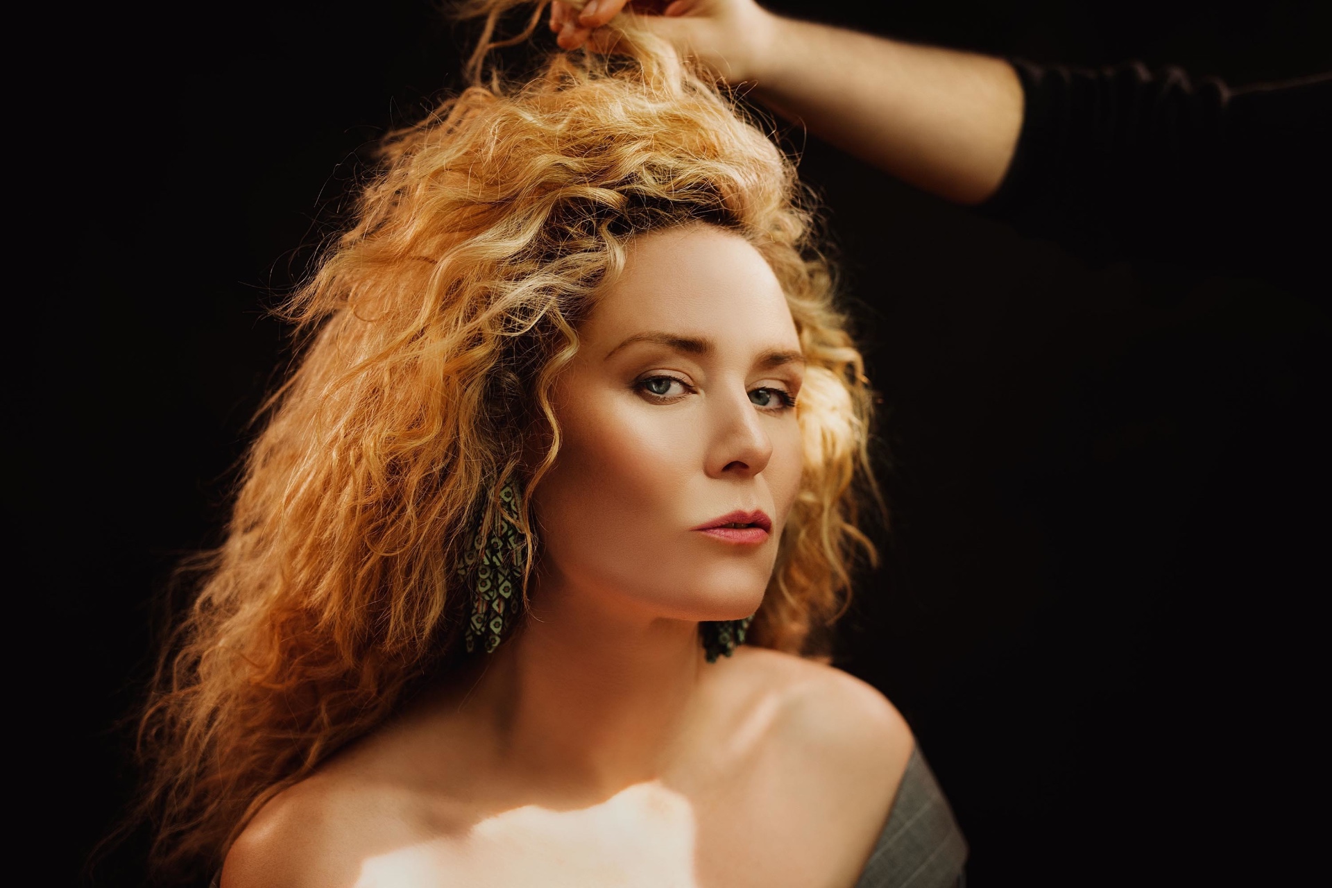 Female singer with curly red hair and elegant earrings in dramatic lighting